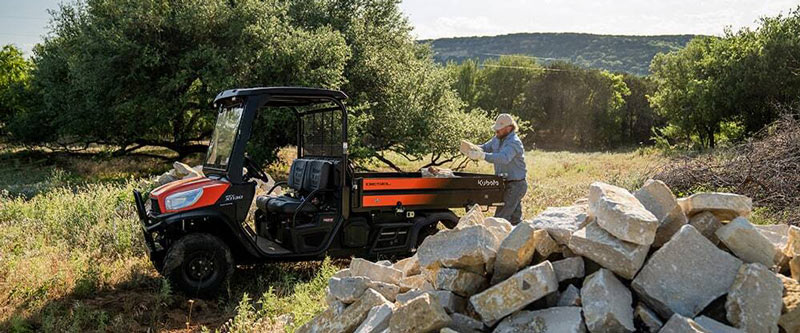 A man standing in a field next to a large pie of rocks. A red Kubota RTV-X1130 utility vehicle is parked next to the pile of rock.